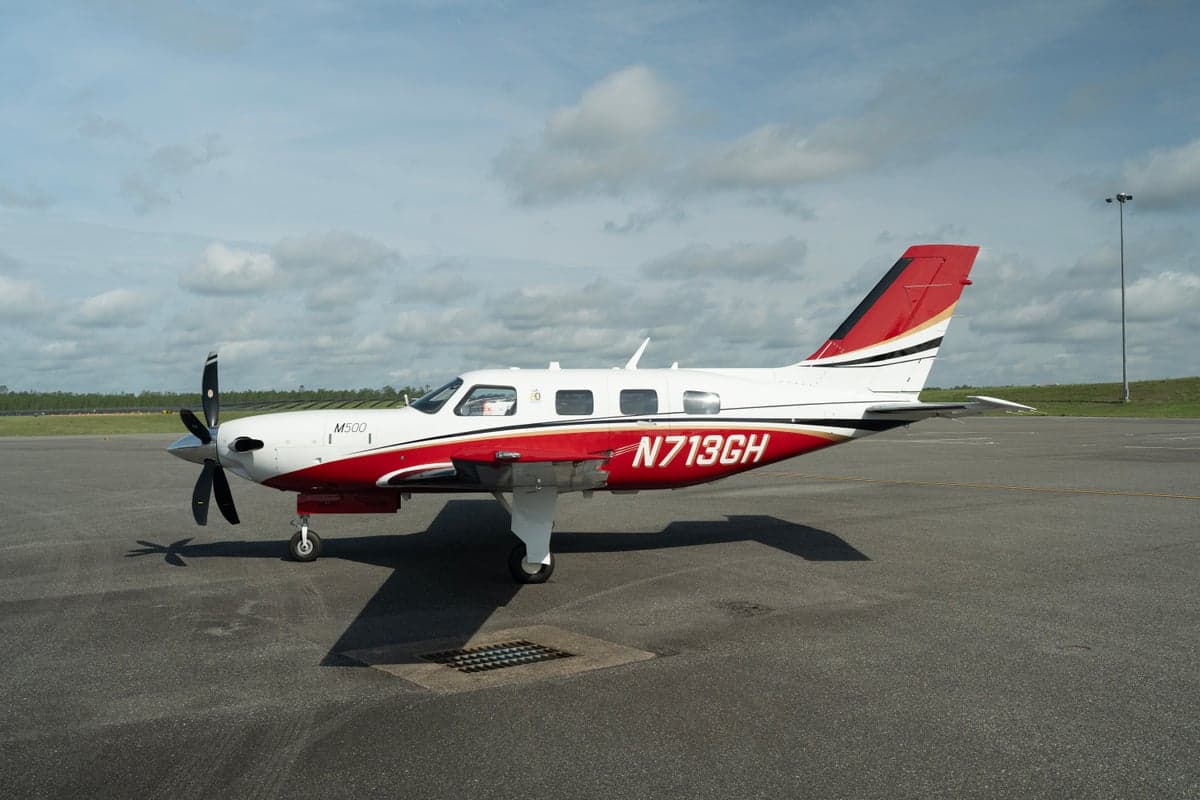 A white and red Piper M500 aircraft with registration N713GH parked on an asphalt tarmac under a partly cloudy sky.