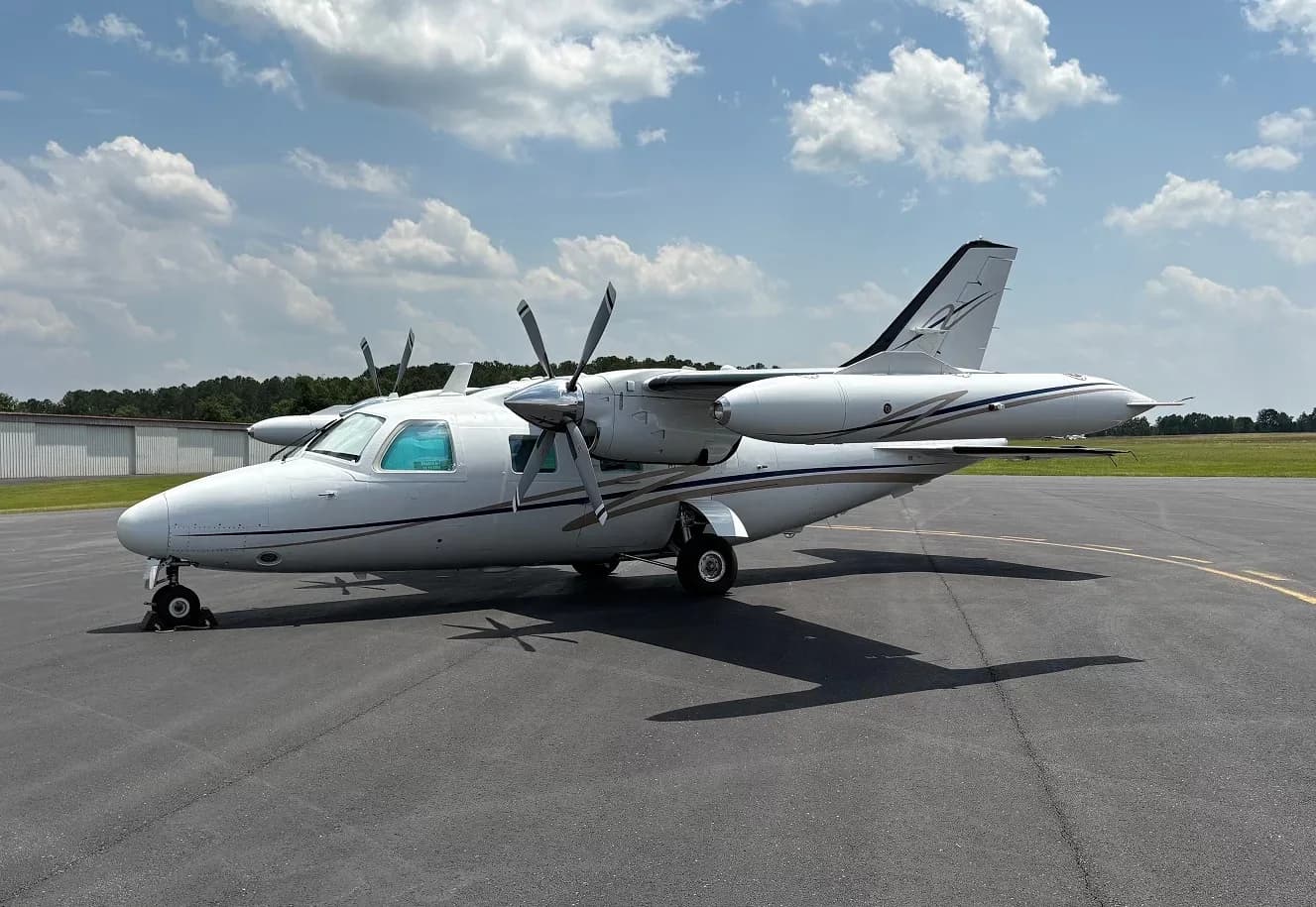 Side view of a white twin-engine aircraft with blue and gold stripes parked on an airfield.