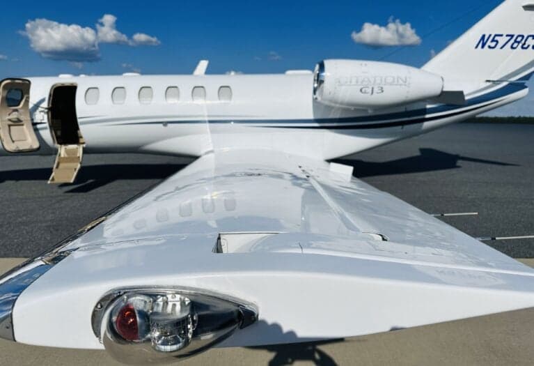 A close-up view of the right wing and tail of a white Cessna Citation CJ3 (N578CJ) with blue and grey stripes, showing the wingtip light and engine.