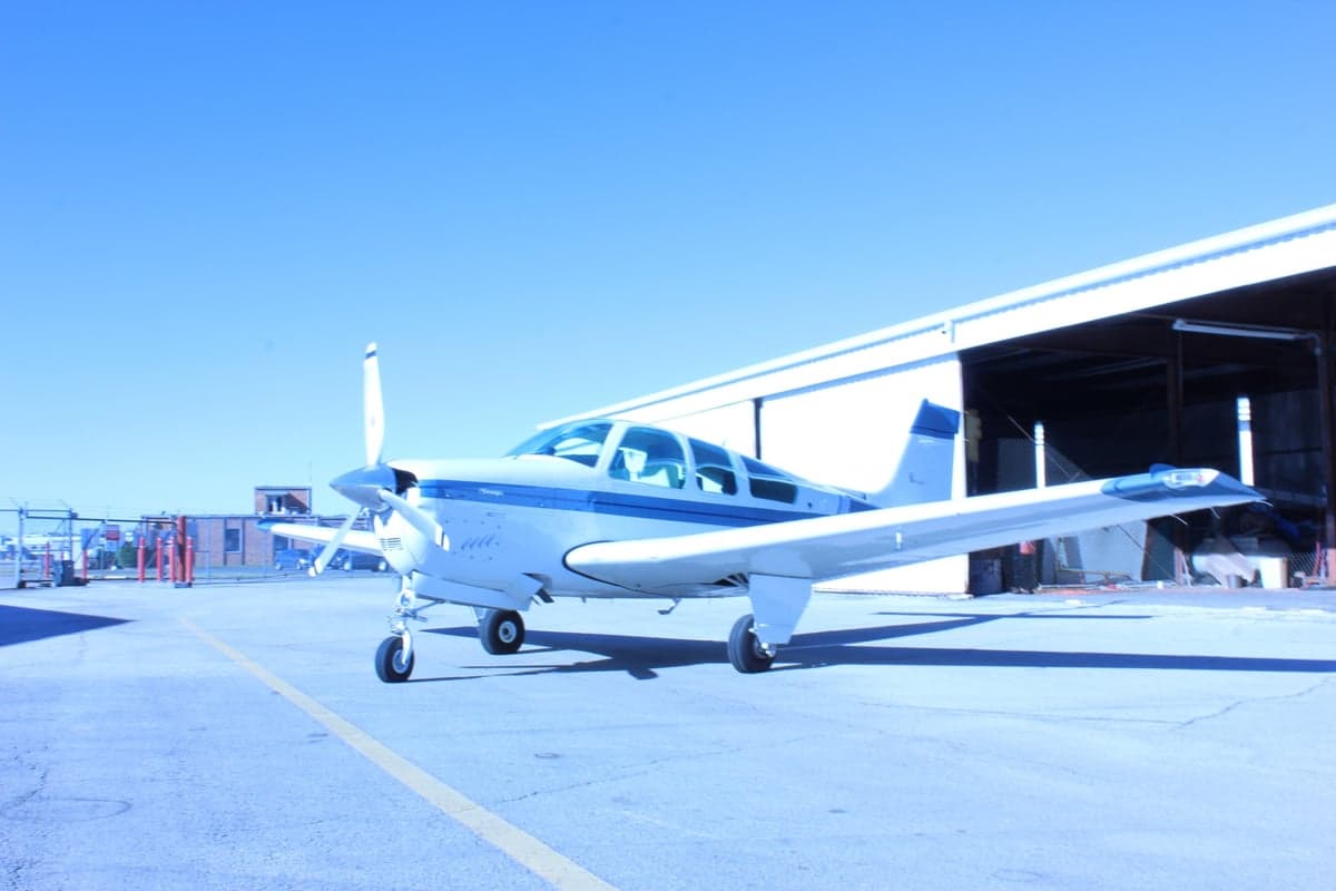 A blue and white single-engine aircraft is parked on the tarmac in front of a hangar.