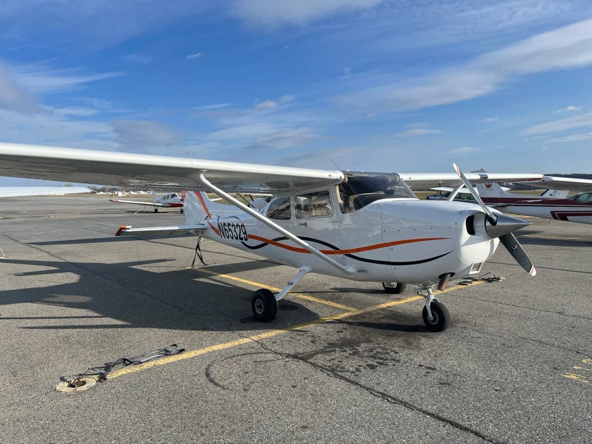 A Cessna 172 Skyhawk with a white and orange paint scheme is parked on the tarmac.