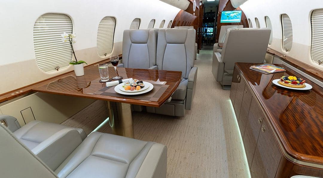 A view of the aircraft's interior, showing leather seats, wood trim, and a table set with food and drinks.