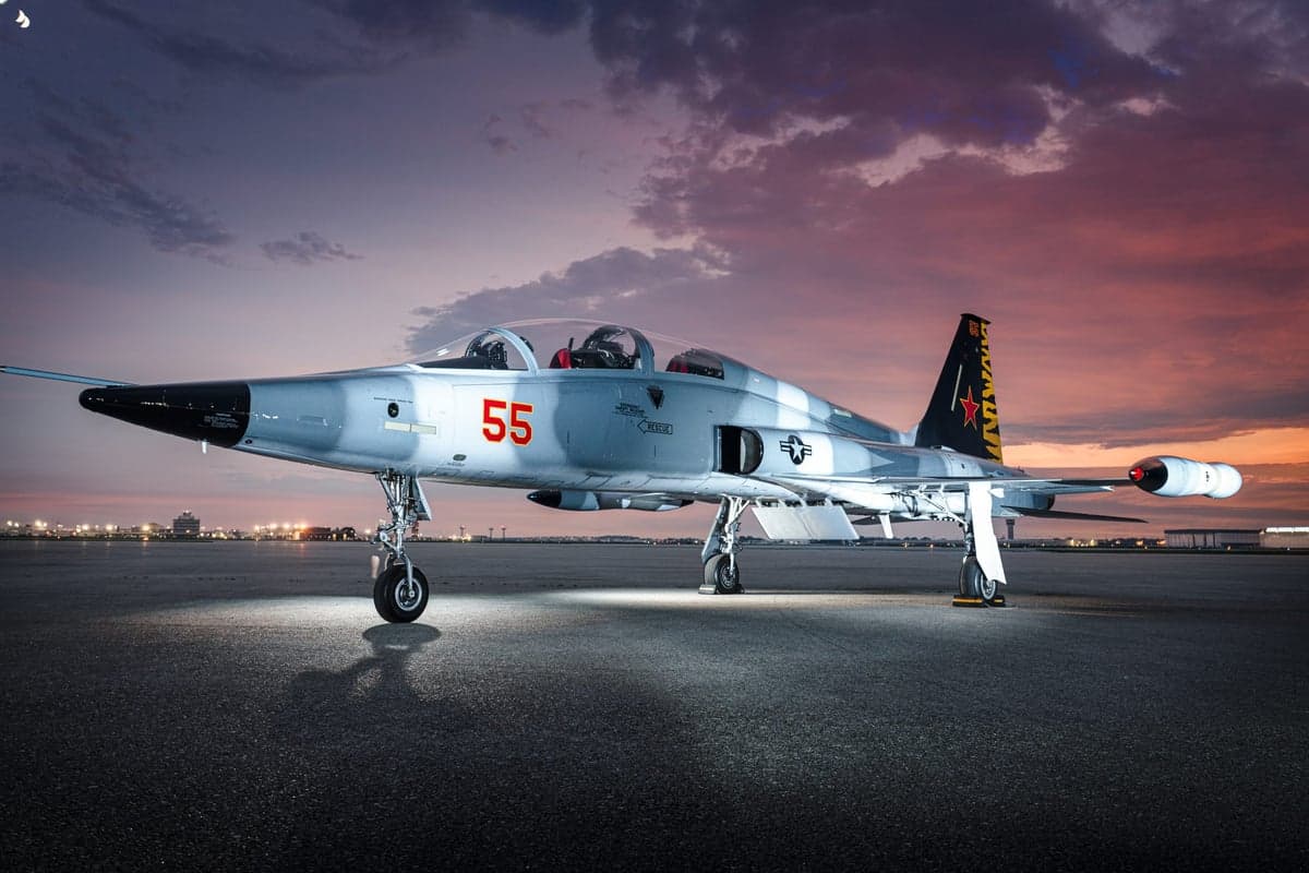 A gray Northrop T-38 Talon with red markings and tail number 55 parked on the tarmac at sunset.