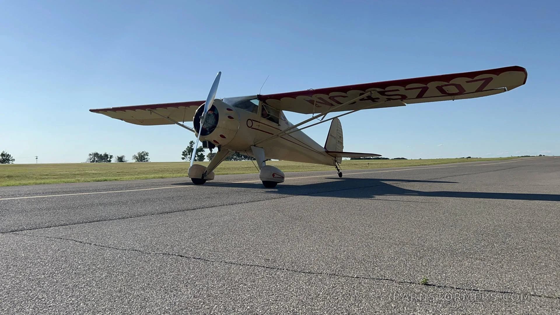 A cream-colored vintage aircraft with red trim on the wings, registration NC45707, is parked on an asphalt runway under a clear blue sky.