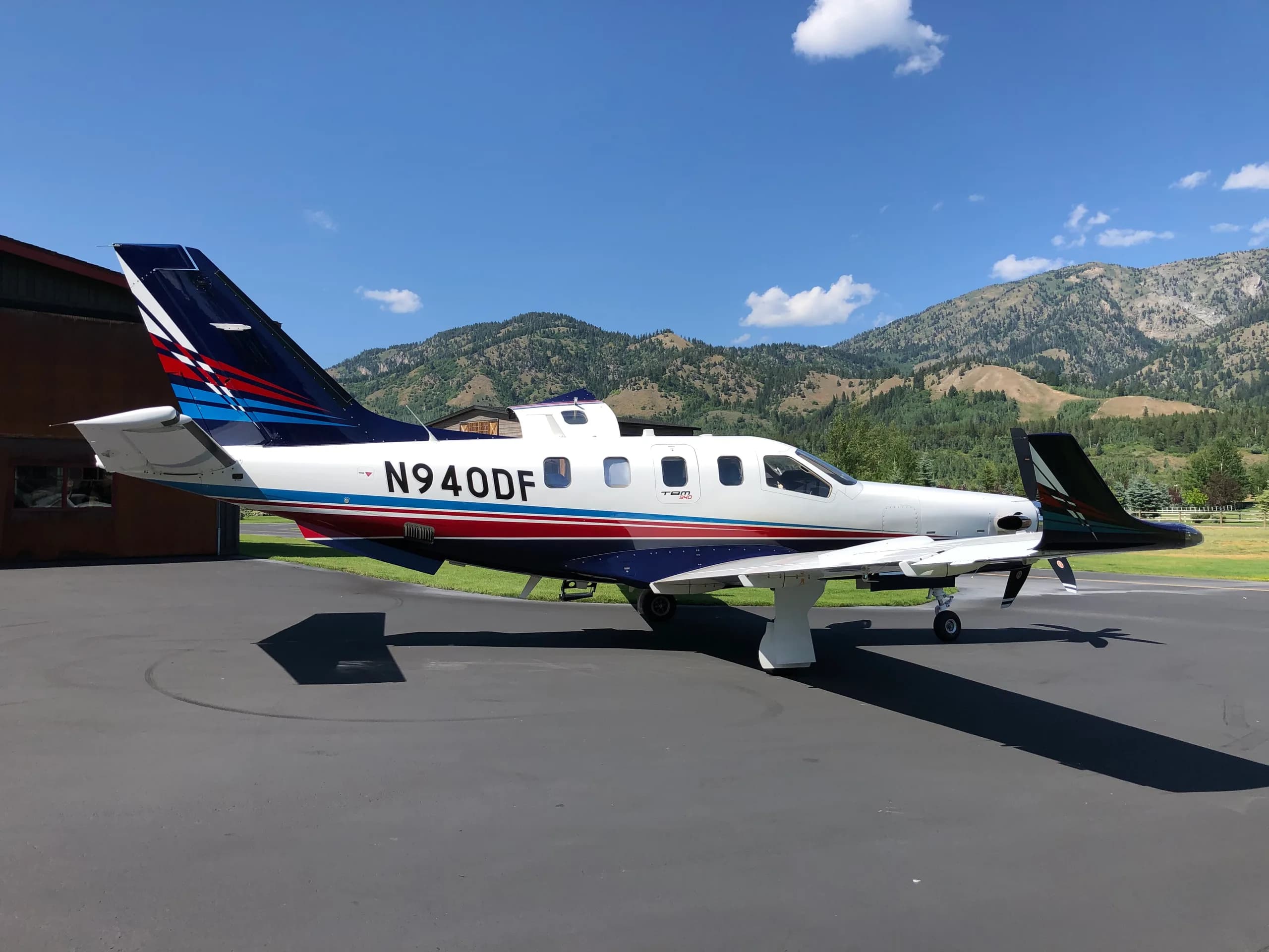 A TBM 940 aircraft with registration N940DF, parked on an asphalt ramp with mountains in the background.