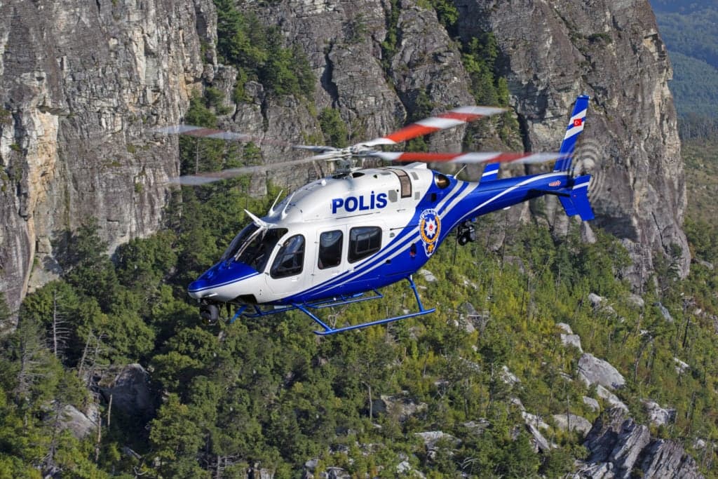 A Turkish police helicopter flies in front of a rocky cliff.