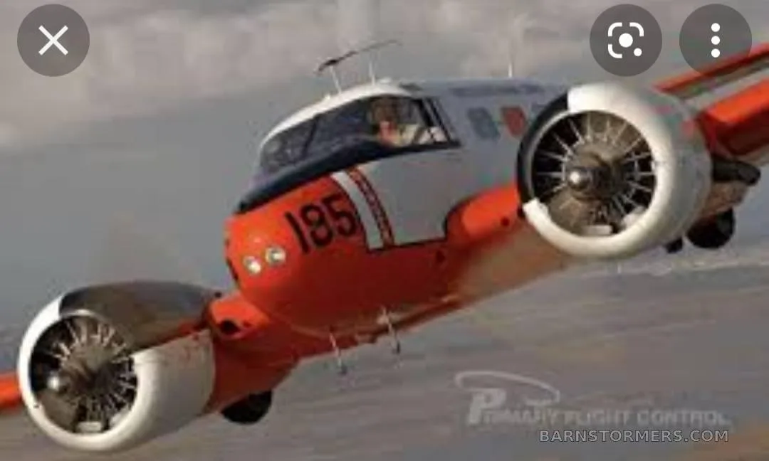 A close-up, dynamic aerial view of the front section of an orange and white twin-engine aircraft with '185' on the nose.