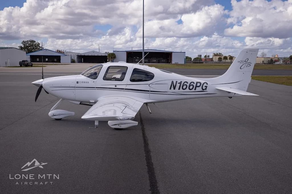 A side view of the white Cirrus SR20 aircraft (N166PG) parked on an airport tarmac.