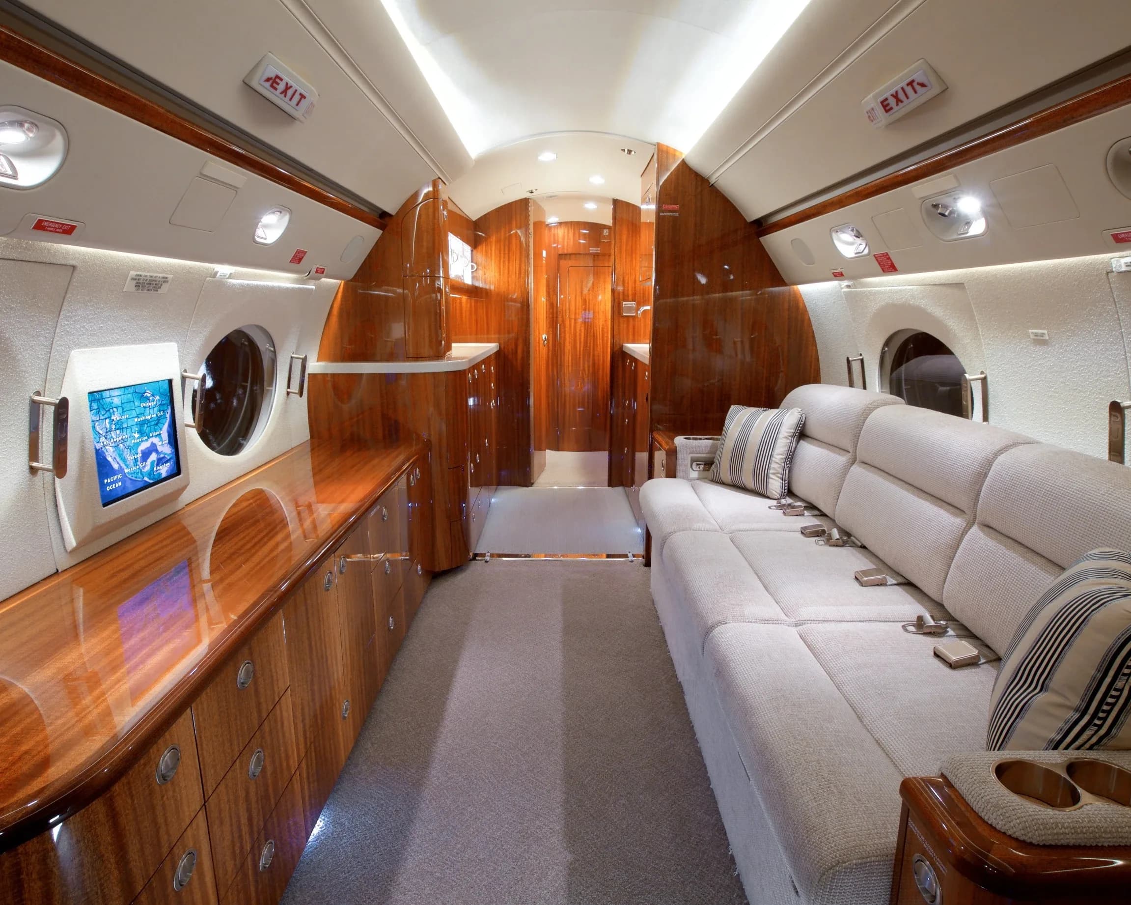 The private jet's spacious cabin features a light-colored sofa with striped pillows and polished wood cabinetry.