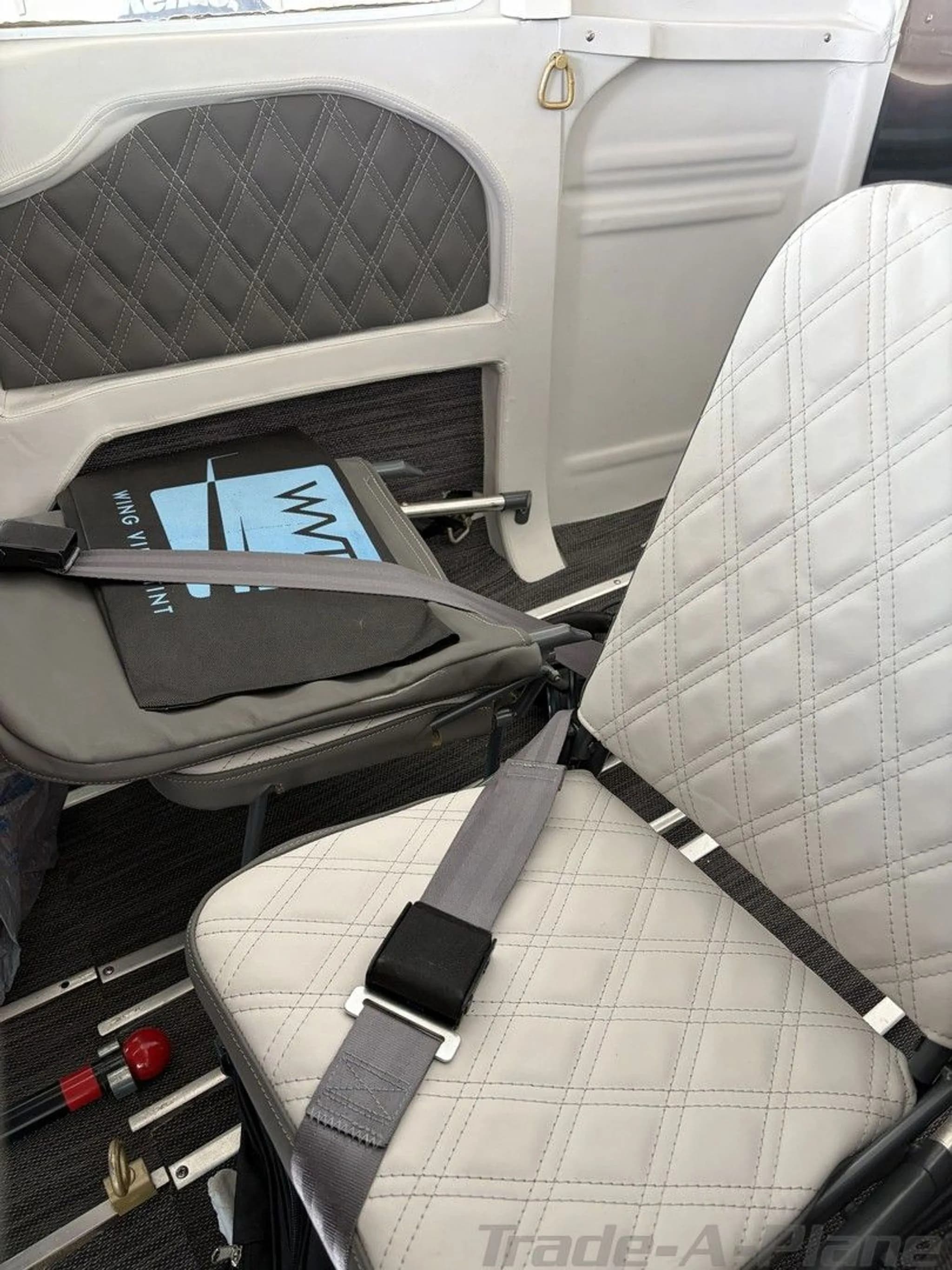 A close-up of the aircraft's interior, showing the quilted grey and white seats and a seatbelt.