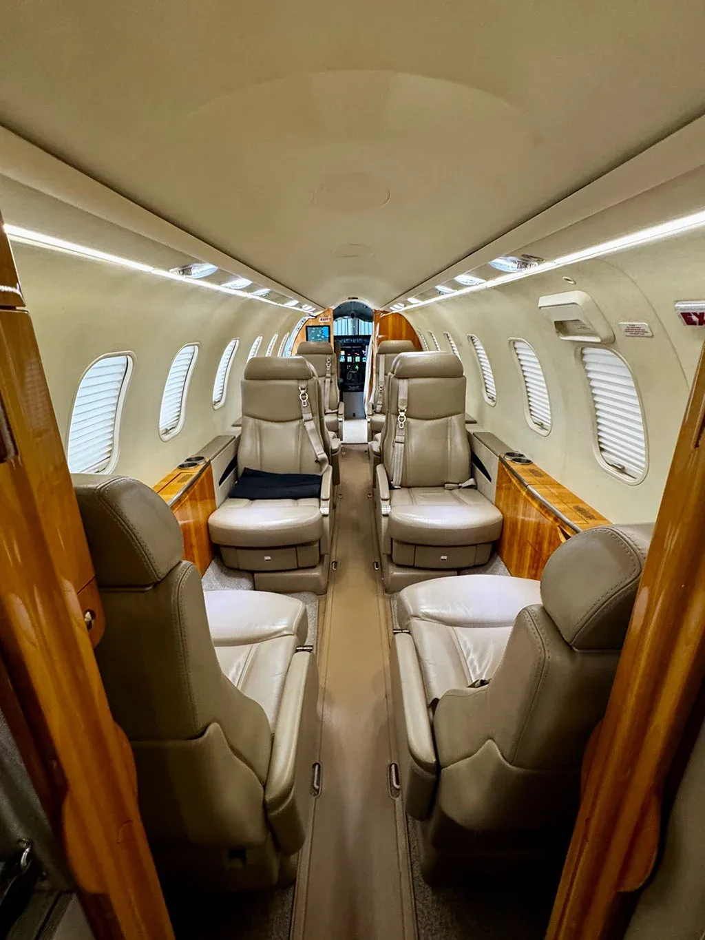The aircraft cabin features a double club seating arrangement with beige leather seats and polished wood trim.