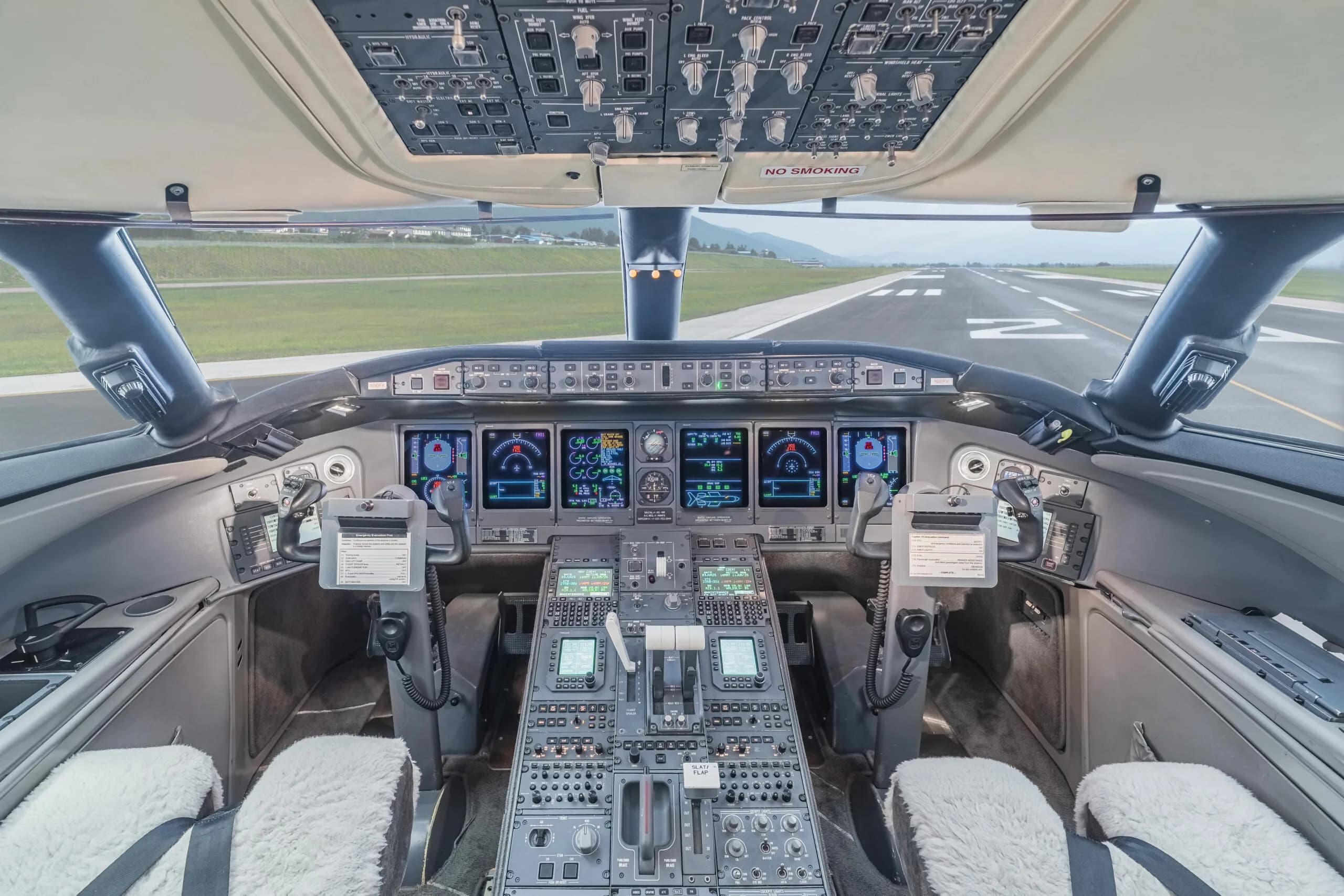 The cockpit of a Bombardier Challenger 605 business jet, showing the instrument panel, controls, and a view of a runway ahead.