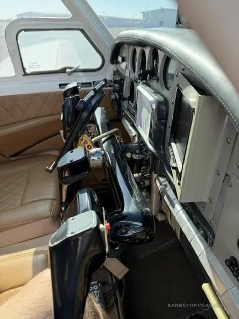 An interior view of an aircraft cockpit showing the control yokes, instrument panel, and tan leather seats.