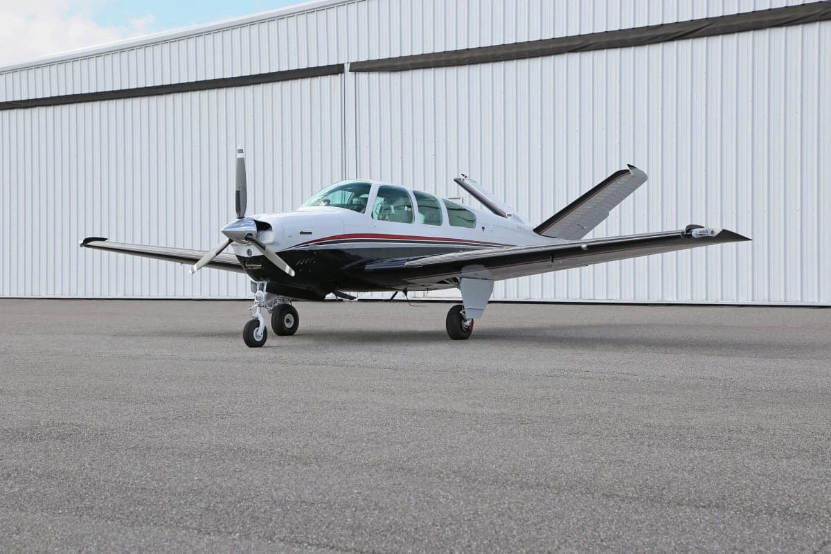 Side view of a Beechcraft Bonanza aircraft on the ground in front of a hangar.