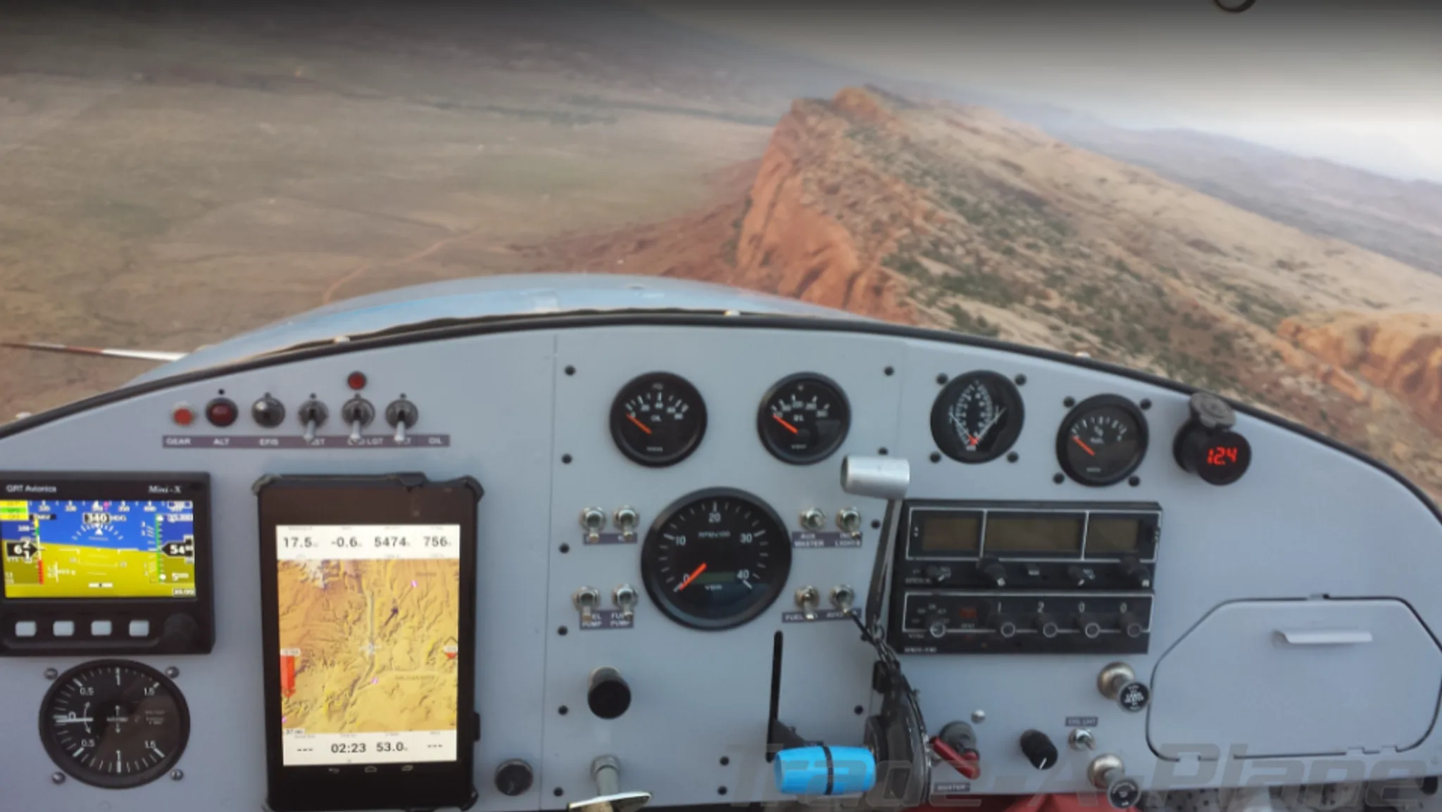 The instrument panel of an aircraft with a tablet display, showing a view of a desert landscape from the cockpit.