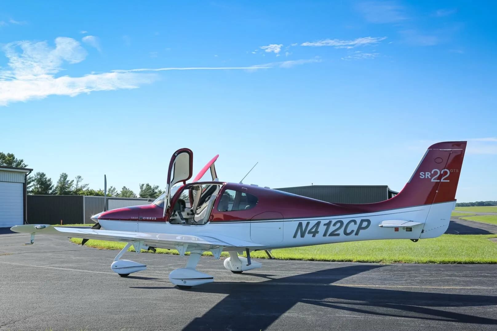 A red and white Cirrus SR22 GTS aircraft (N412CP) with its doors open, parked on an airfield.