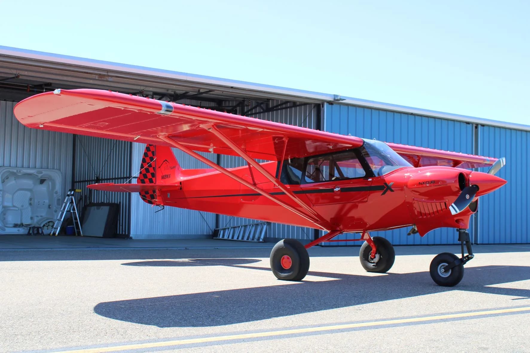 Full side view of the red NX Cub aircraft parked on the tarmac.