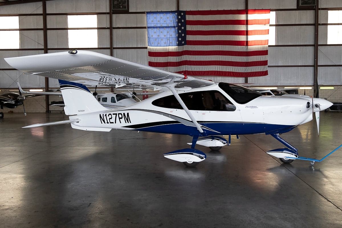 Tecnam P2010 aircraft with blue and white paint scheme in a hangar.