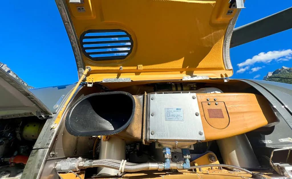 An open access panel reveals the engine and internal components of a grey helicopter.