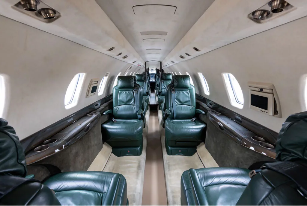 The interior cabin of a private jet with dark green leather seats and light-colored walls.
