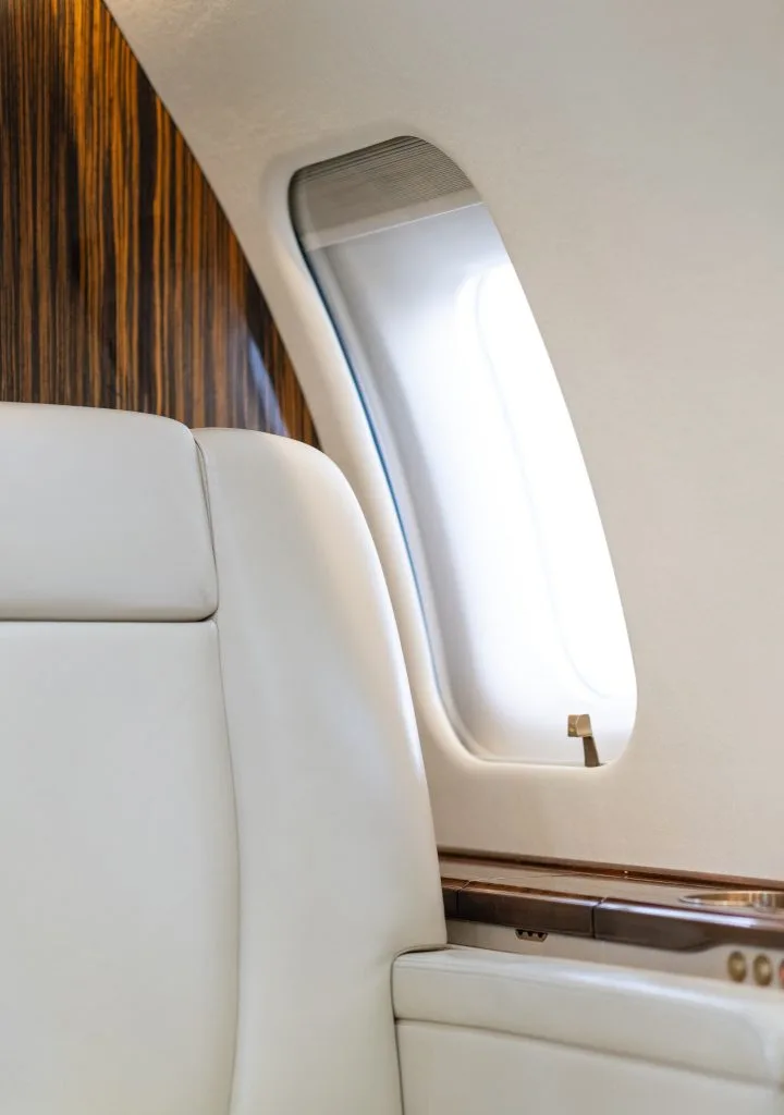 The rear section of the business jet's cabin, showing a long sofa and cream leather seats.