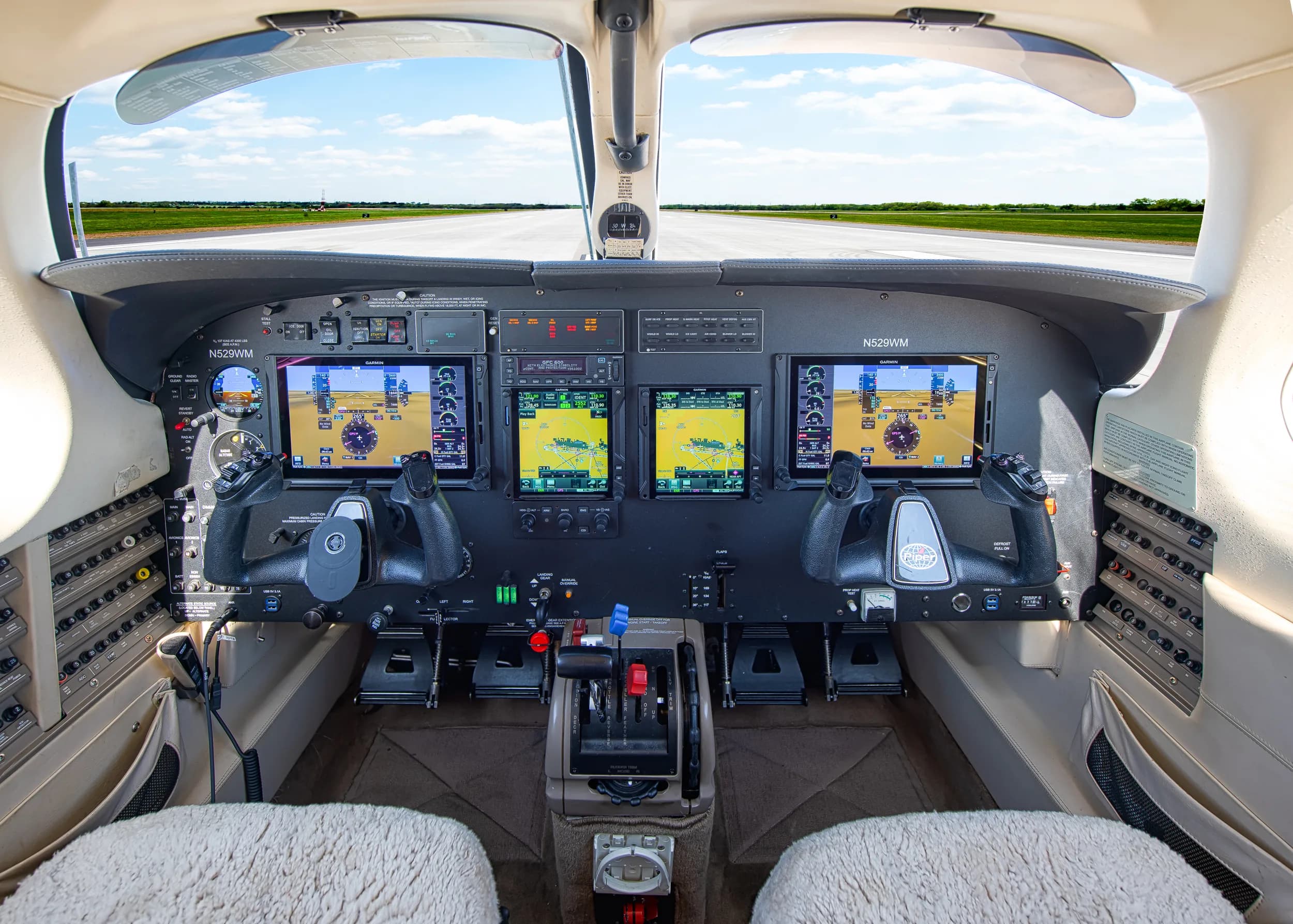 A wide view of the modern glass cockpit of the N529WM aircraft, showing multiple display screens and controls, with a runway visible through the windshield.