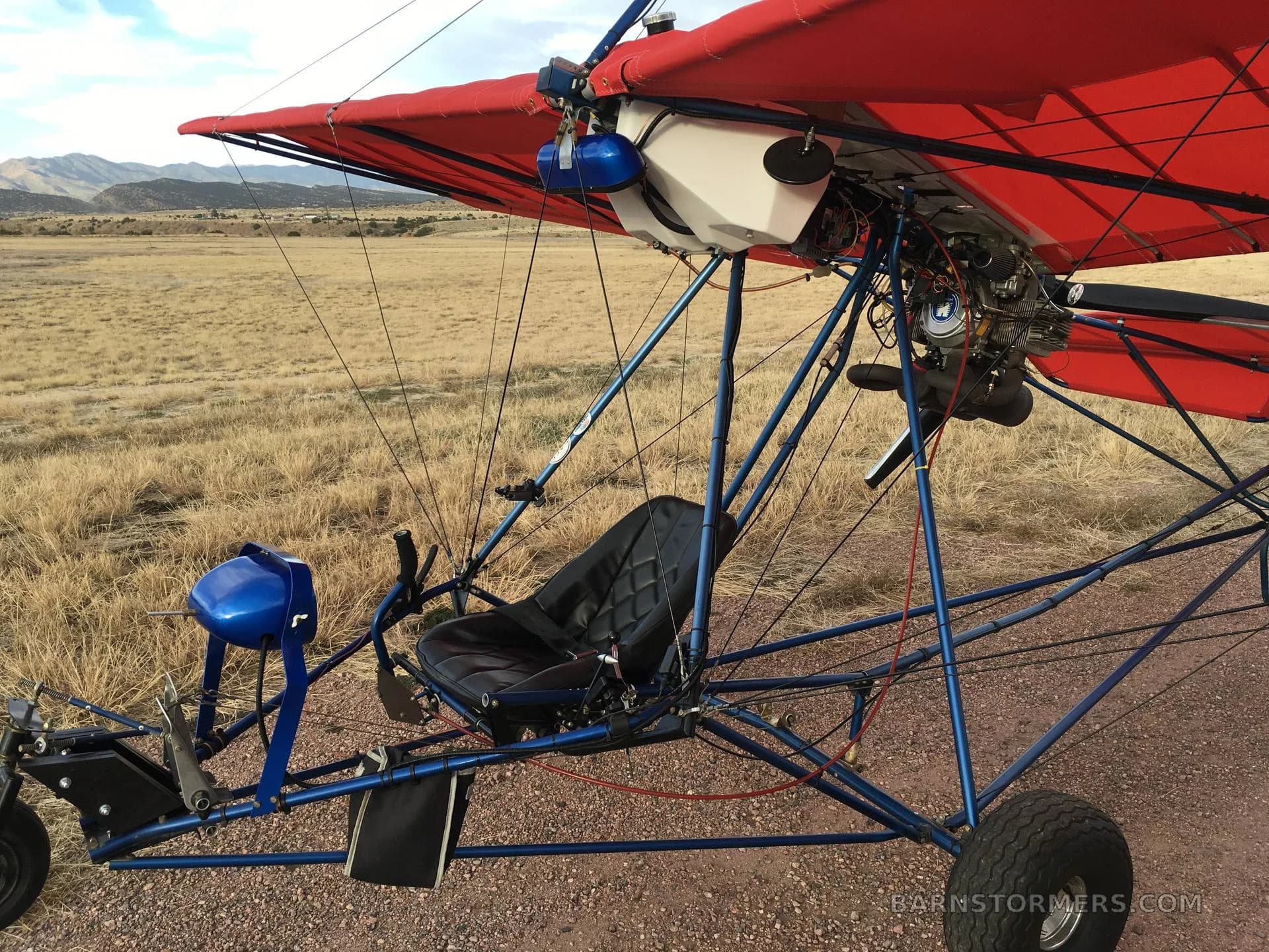 A close-up view of the black pilot's seat and blue frame of a red ultralight aircraft.