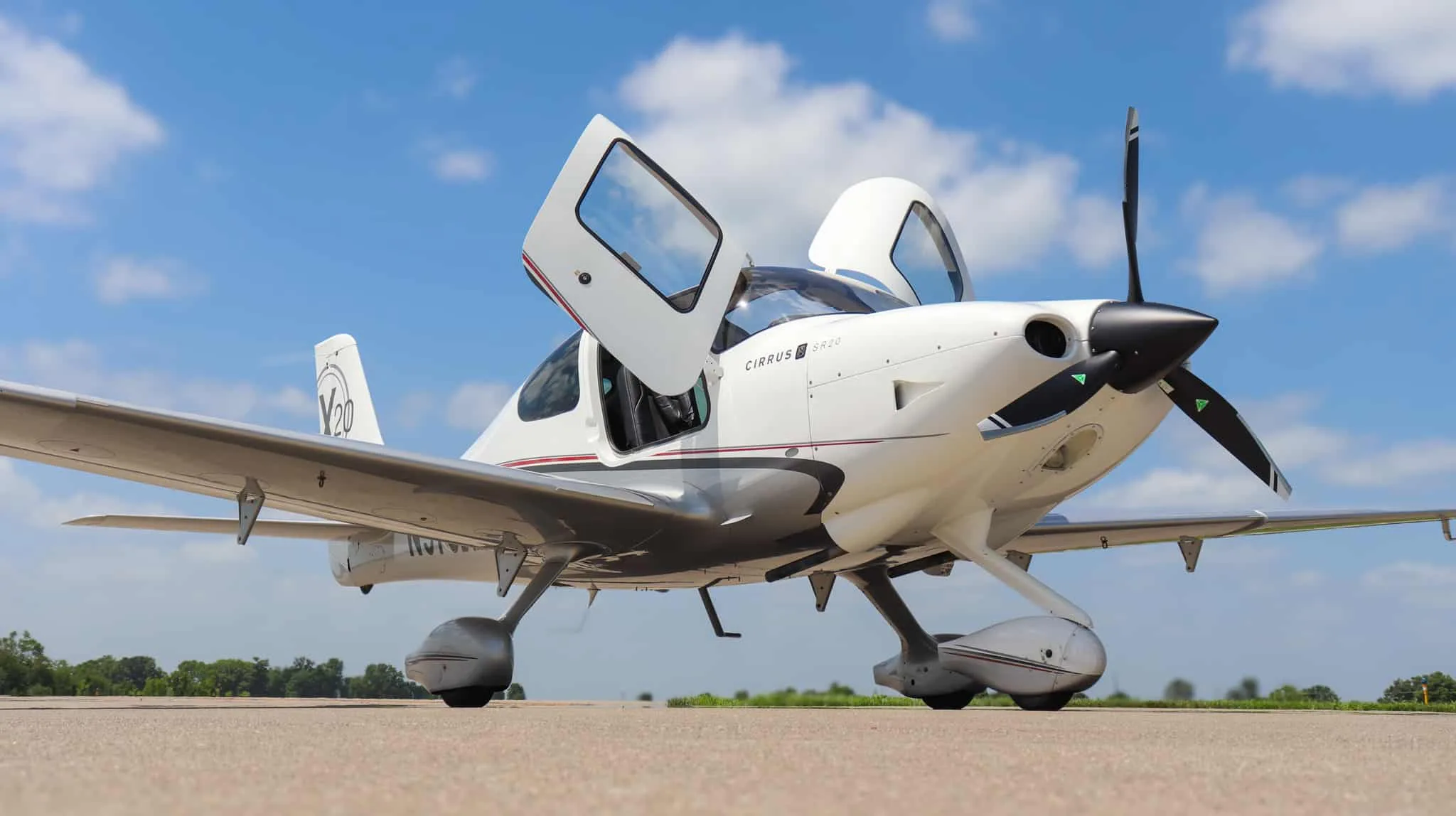 A white Cirrus SR20 X Edition aircraft with open doors, parked on an airfield under a blue sky.