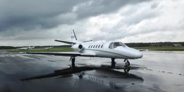 A white Cessna CitationJet with green stripes on a wet tarmac.