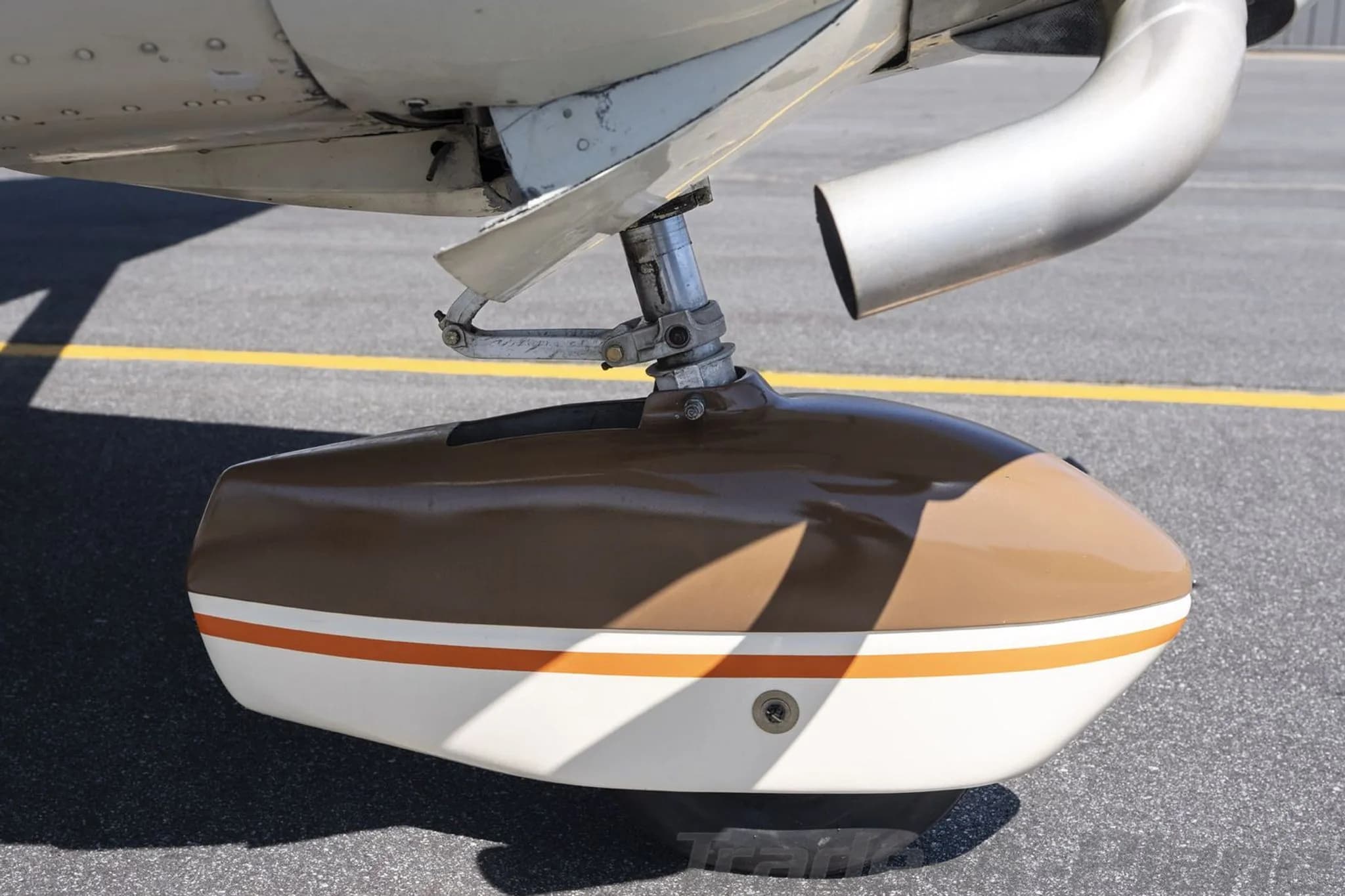 A close-up of the brown and white main landing gear fairing with an orange stripe, showing the exhaust pipe above.