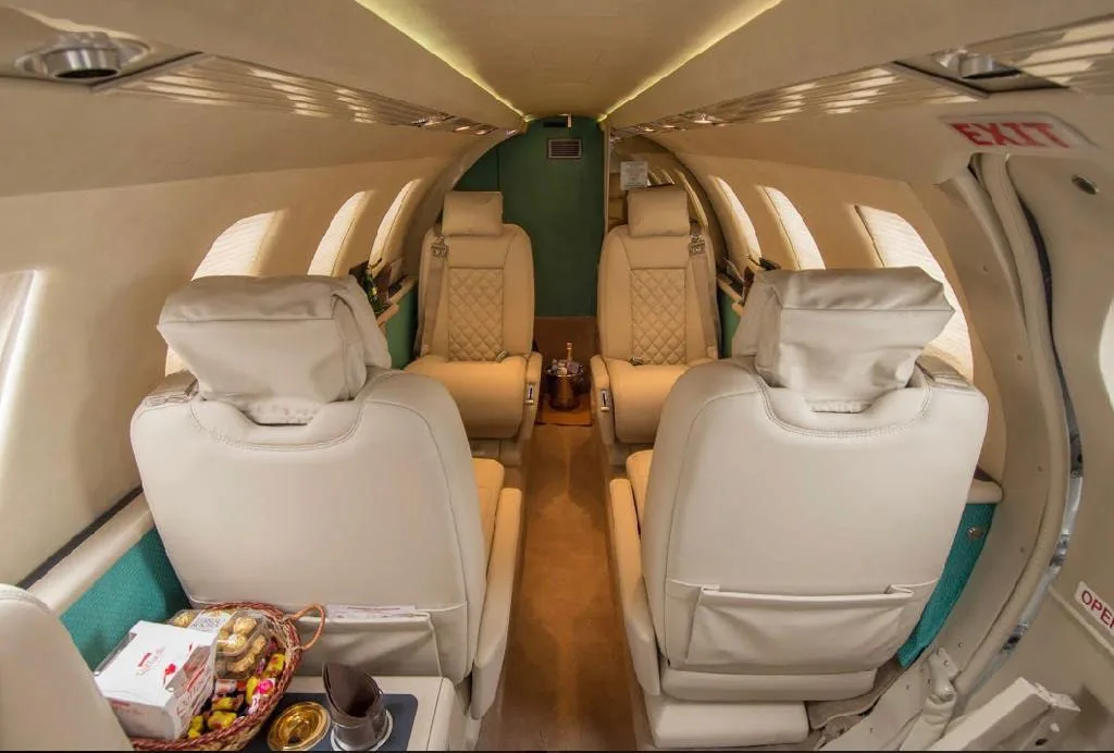 The full cabin interior of a private jet, showing multiple rows of beige quilted seats and an exit sign above the door.