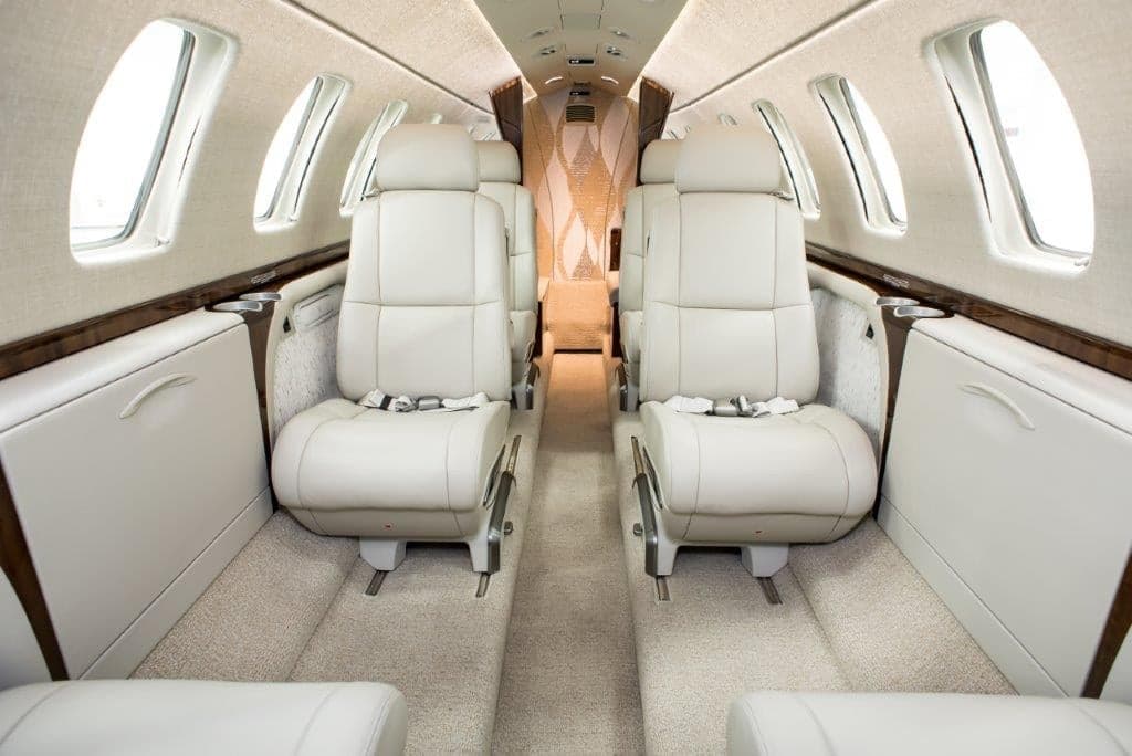 The luxurious interior cabin of a business jet with light-colored leather seats and a patterned bulkhead.