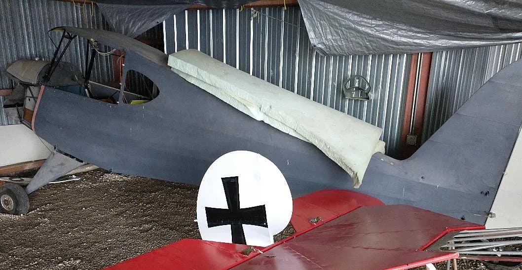 The rear fuselage and tail of a grey aircraft, with a red wing featuring a white circle and black German cross insignia.