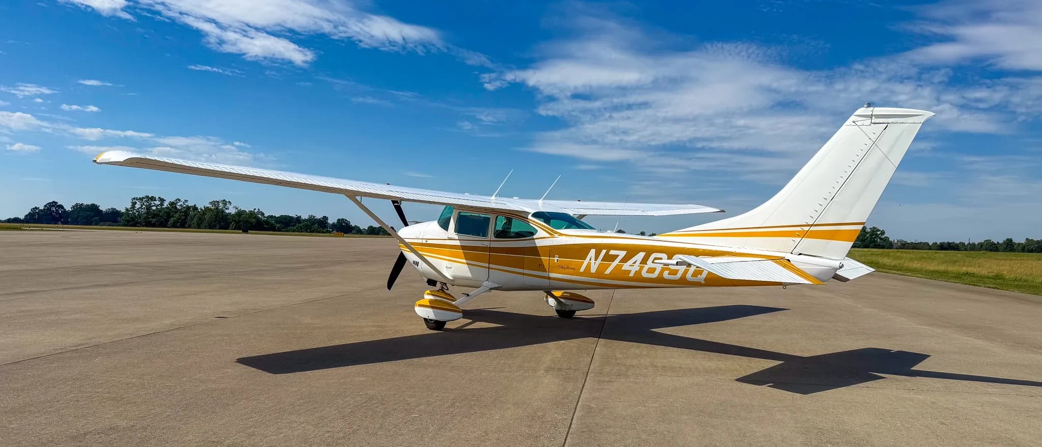 A white and gold Cessna Skylane N7489Q is parked on an airfield tarmac, viewed from the right-rear side.