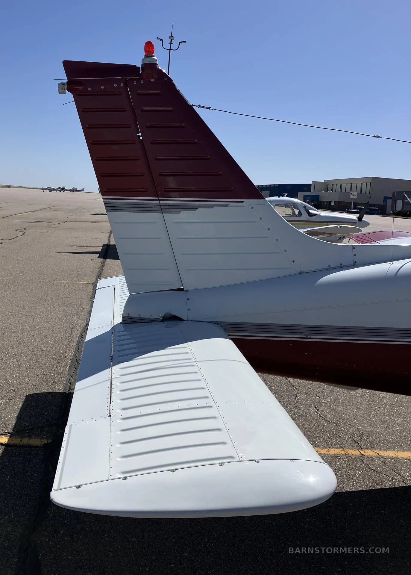 A close-up view of the white and maroon tail and right wing of a Piper Arrow aircraft.