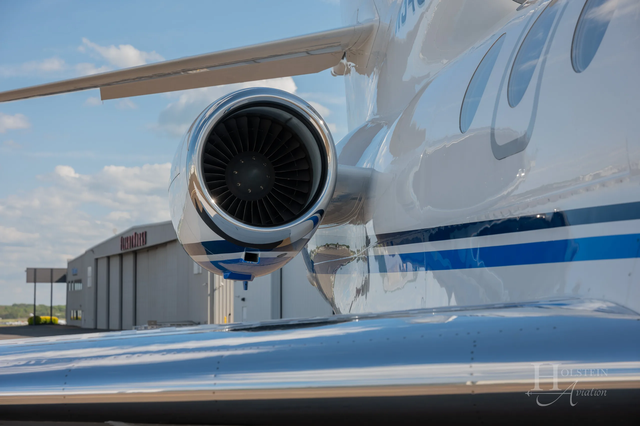 A close-up view of the rear-mounted engine and wing of the white Dassault Falcon 900EX, N346EX, with a blue stripe.