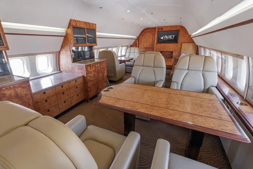 A view of the aircraft's luxurious interior cabin with beige seating, wooden cabinetry, and a dining table.