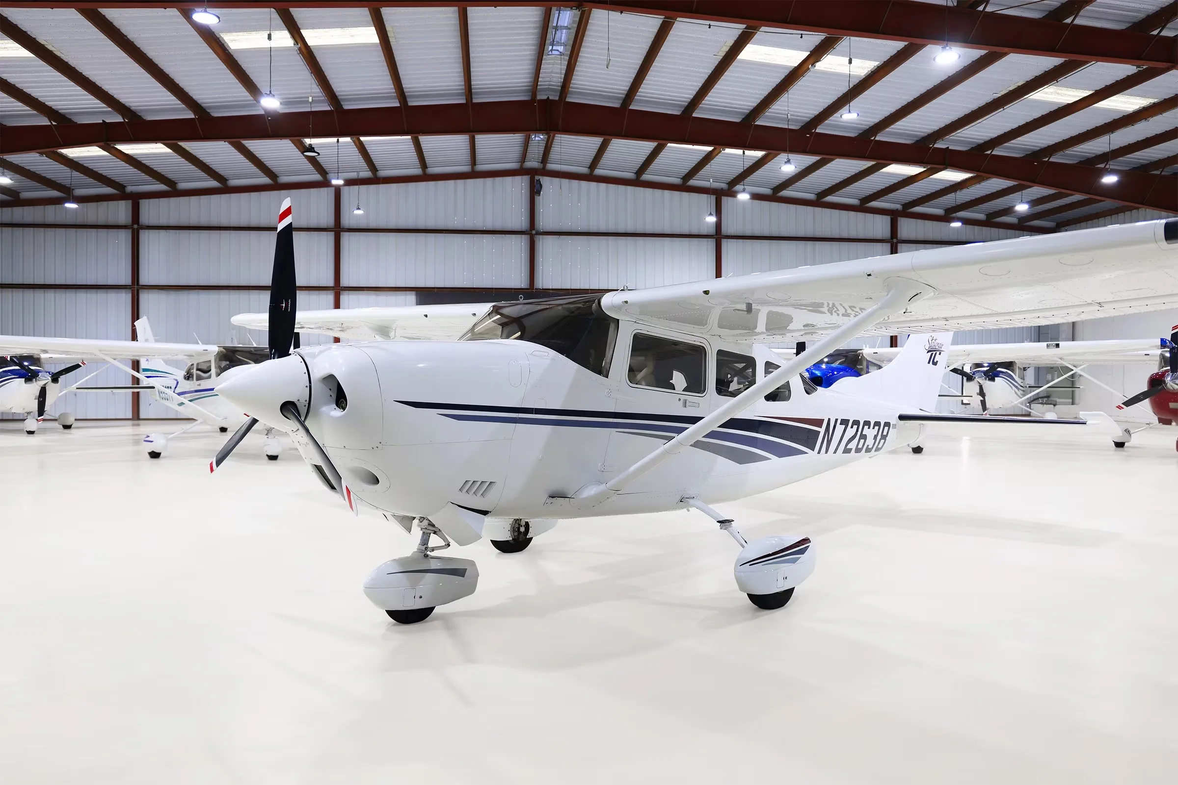 A front-side view of a white Cessna Stationair TC aircraft (N72638) with blue and gray stripes in a hangar.