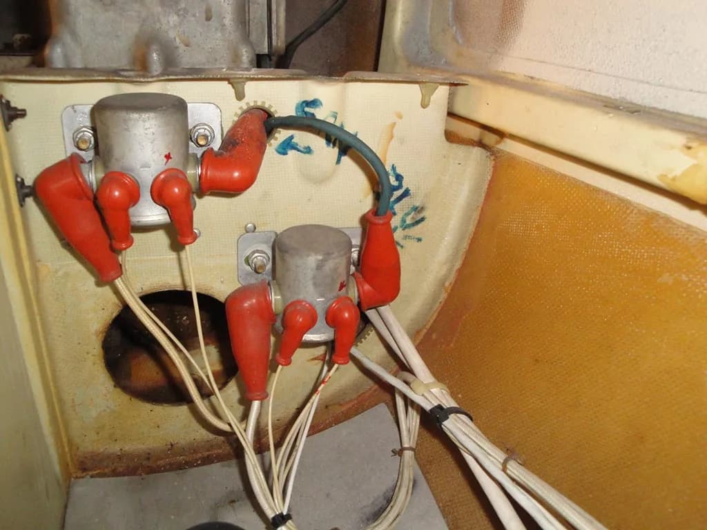 A close-up view of aircraft wiring with red protective boots connected to cylindrical components, against a beige internal panel.