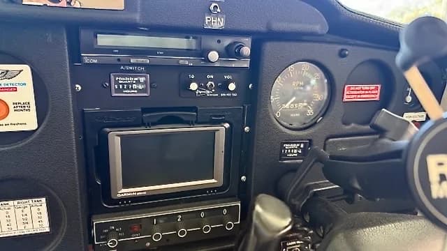 A close-up view of an aircraft's center instrument panel, featuring a radio, hour meter, and a Garmin GPS unit.