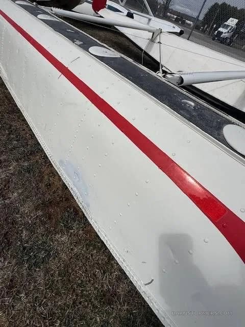 A very close view of the side of a white aircraft float, showing rivets and a red stripe.