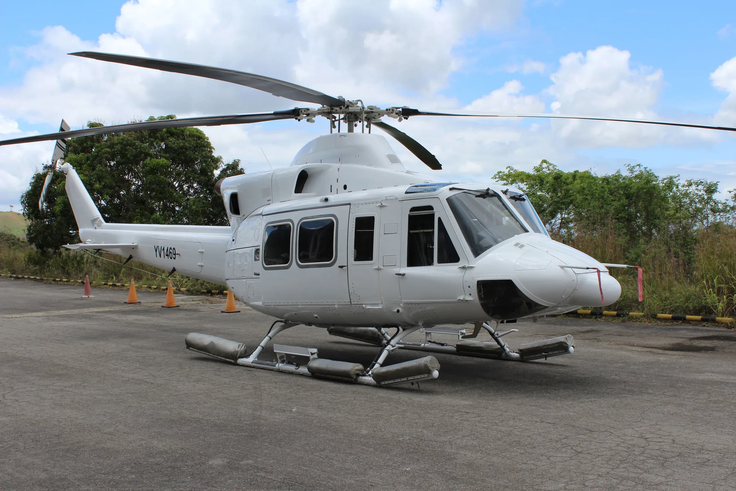 A white Bell 412 helicopter parked on an asphalt pad with trees in the background.