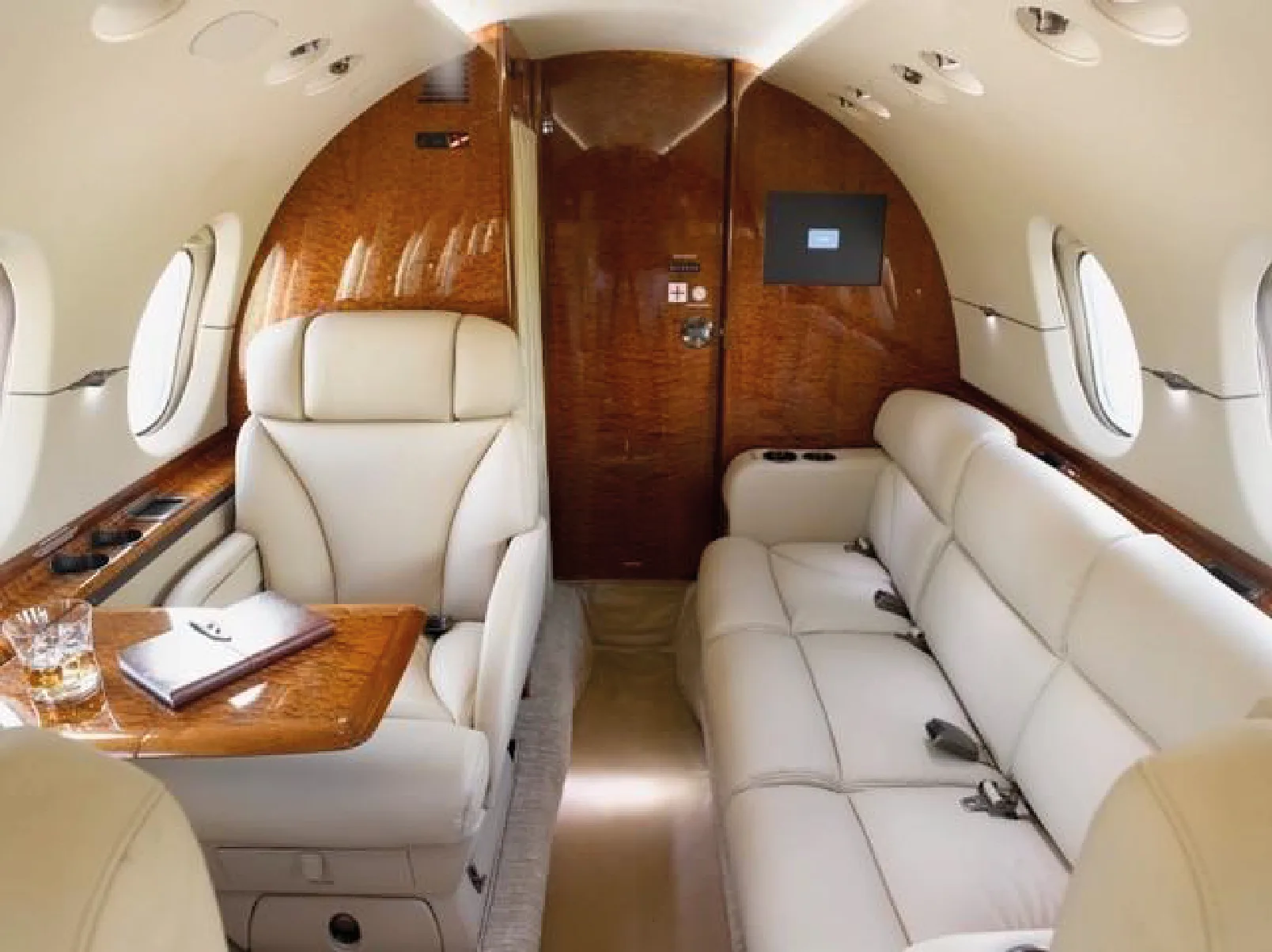 Aircraft interior with cream-colored leather seats, wood trim, and a small table.