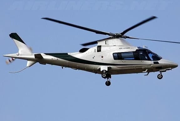 A silver and green helicopter flies in the sky.