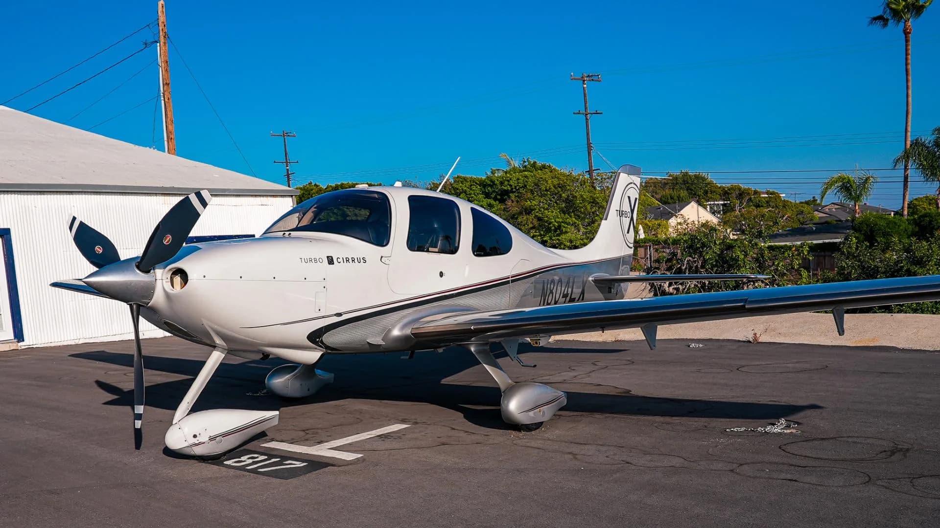 A white and silver Cirrus SR22T aircraft with registration N804LX parked on an asphalt apron.
