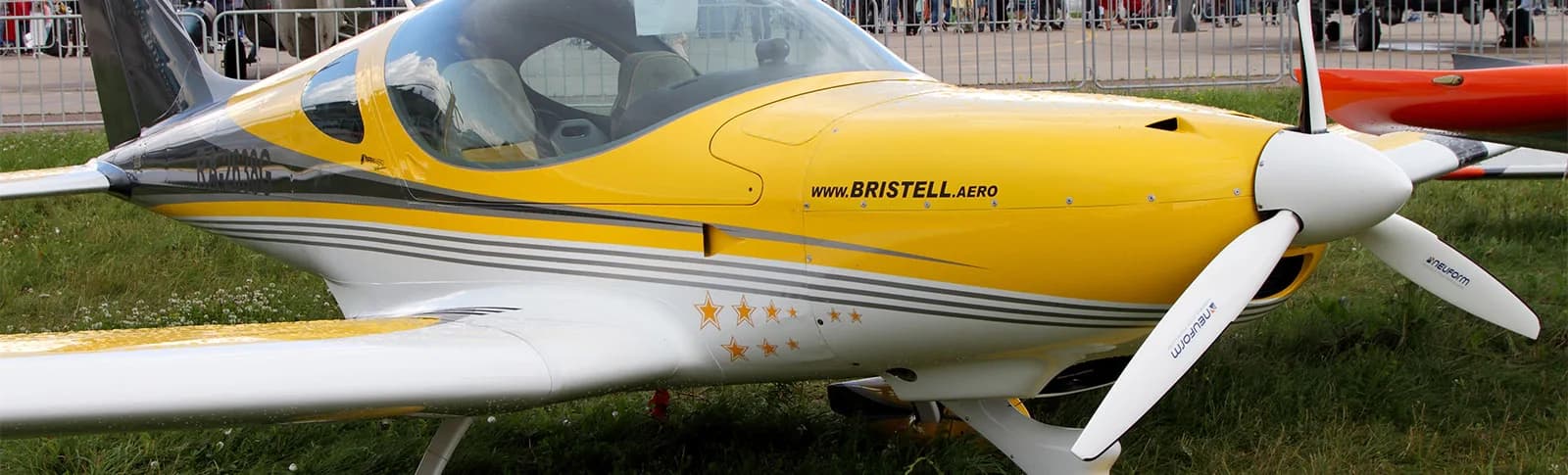 Close-up of a yellow and white Bristell aircraft on the ground.