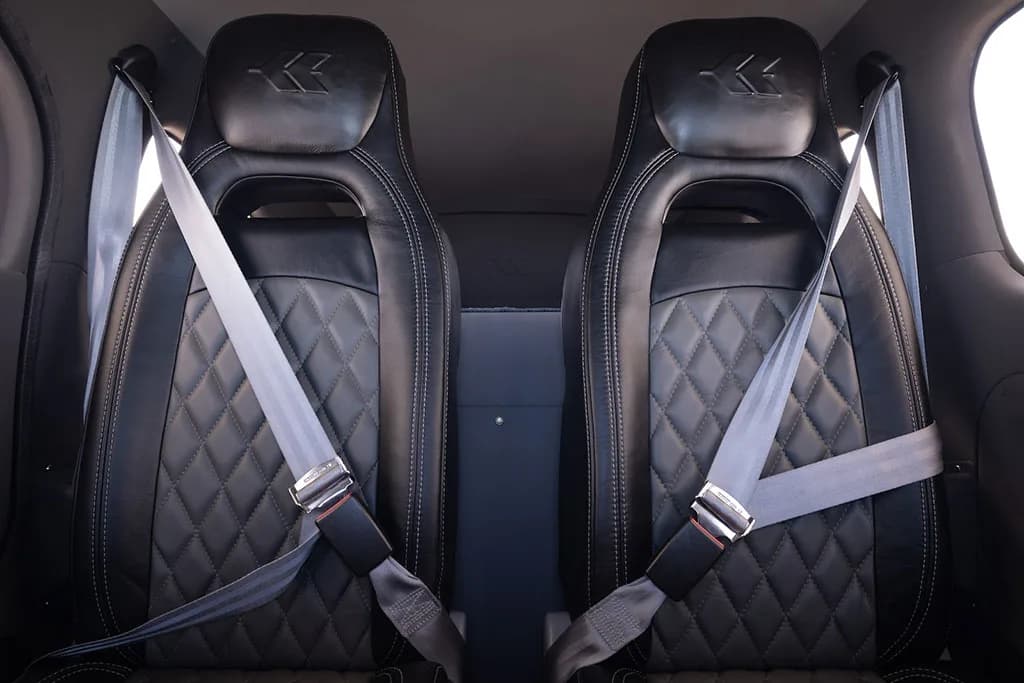 Two black leather aircraft seats with quilted stitching and grey seatbelts in the cabin.