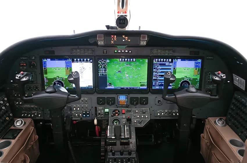 The modern glass cockpit of a business jet, featuring multiple large display screens and control yokes.