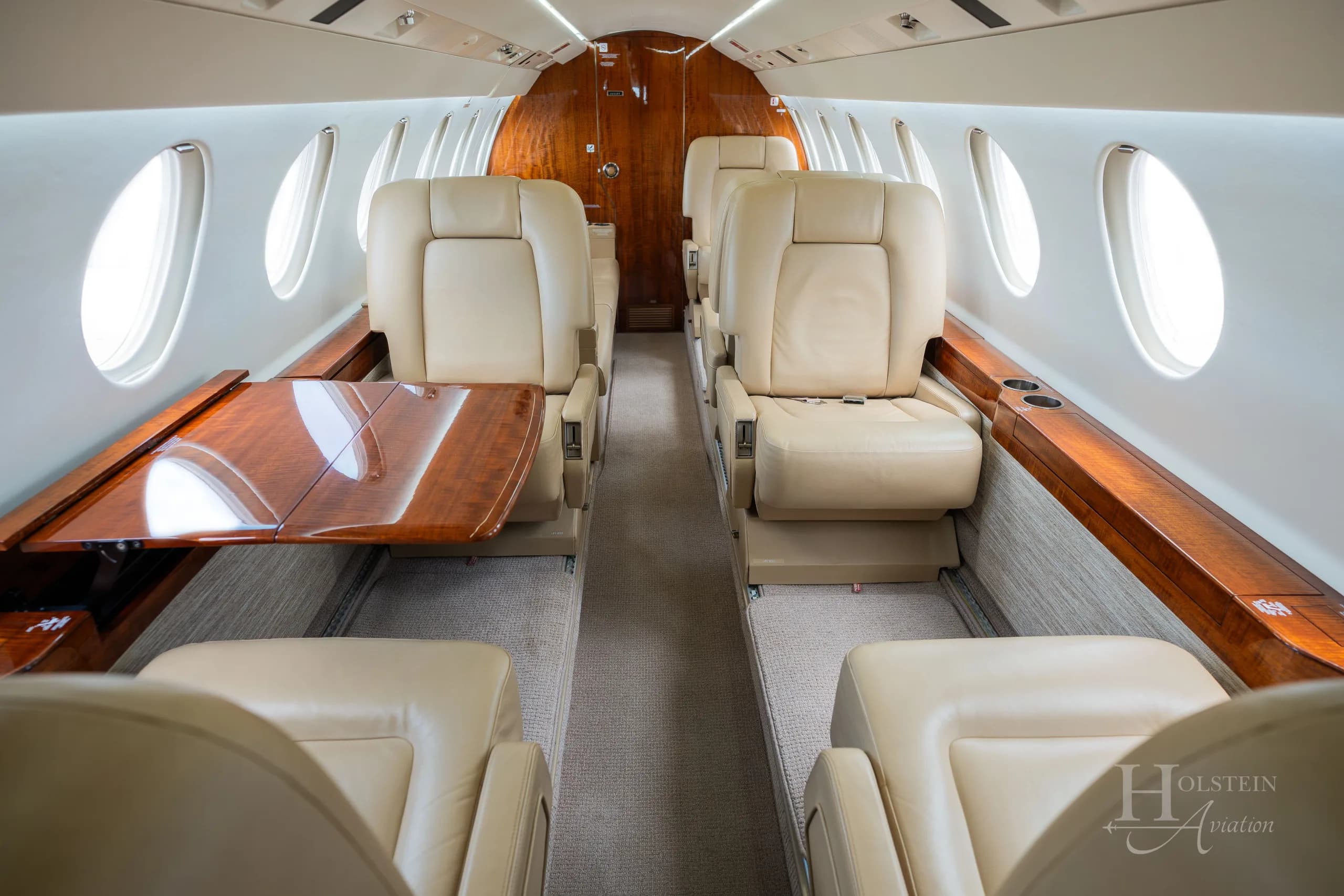 The cabin interior of the Dassault Falcon 900EX, showing beige leather seats and a polished wooden fold-out table.