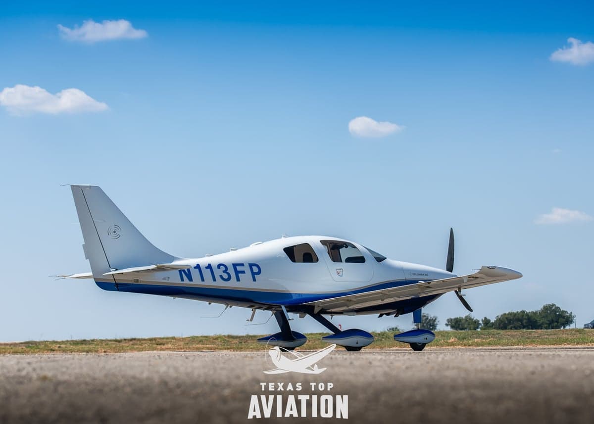 A Columbia 400 aircraft is parked on the tarmac with a white and blue paint scheme.